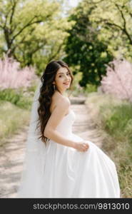 a young girl bride in a white dress is spinning on a path in a spring forest on a wedding day