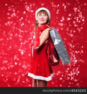 a young girl dressed as Santa Claus on a red background is engaged in shopping. A girl holding shopping bags. Happy New Year and Merry Christmas!
