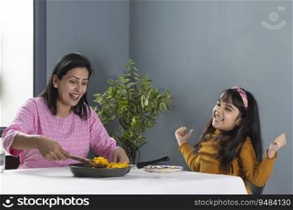 A YOUNG GIRL EXPRESSING HAPINESS OVER FOOD BEING SERVED BY MOM