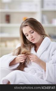 A young girl in a bathrobe looking at the hair ends