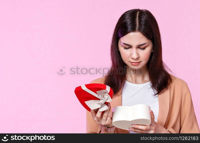 a young girl in a light jacket with a gift box in her hands. dissatisfied and disappointed . on a pink isolated background.