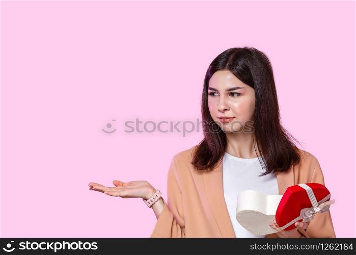 a young girl in a light jacket with a gift box in her hands. dissatisfied and disappointed . on a pink isolated background.