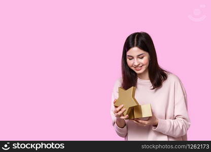 a young girl in a light sweater with a gift box in her hands. surprised and happy with the gift. on a pink isolated background.