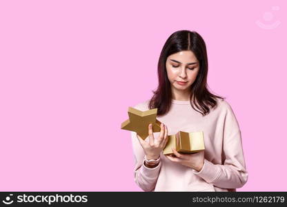 a young girl in a light sweater with a gift box in her hands. dissatisfied and disappointed . on a pink isolated background.