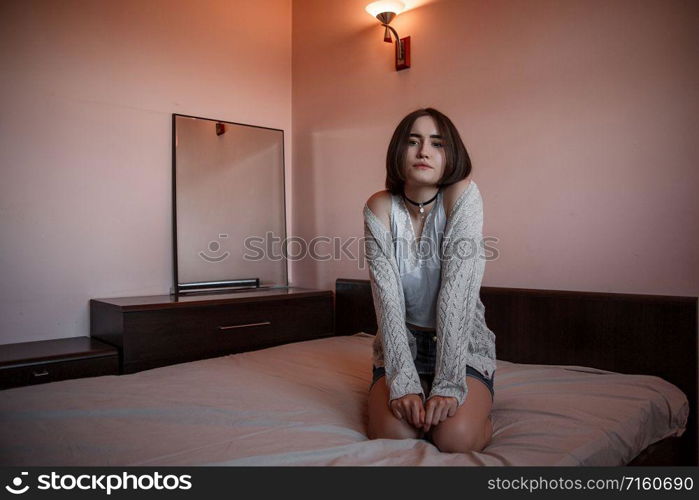 a young girl in a short skirt and a white blouse sits on the bed with a sad and thoughtful face