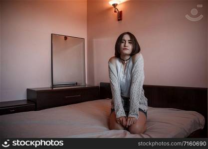 a young girl in a short skirt and a white blouse sits on the bed with a sad and thoughtful face