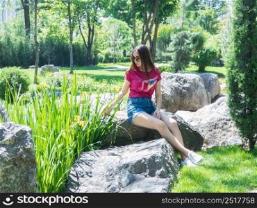 a young girl is sitting on a large rock in a picturesque park in sunny day. the girl of Asian appearance. young girl in a picturesque park