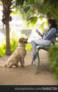 A YOUNG GIRL READING BOOK WHILE PET DOG OBEDIENTLY LOOKING AT HER