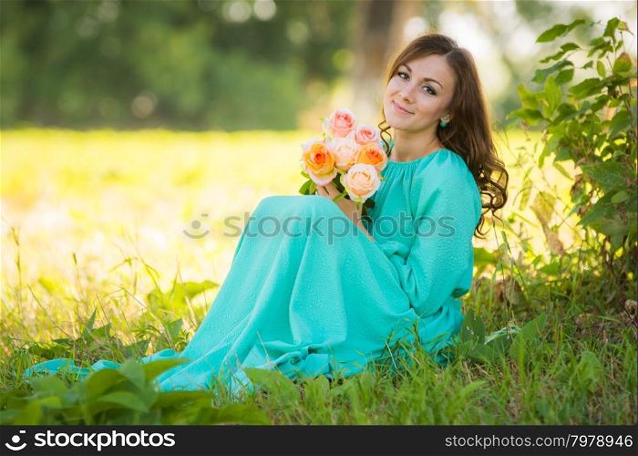 A young girl sits with a bouquet of flowers under the shade of trees on a sunny day. The young beautiful girl walks in autumn forest in warm sunny weather