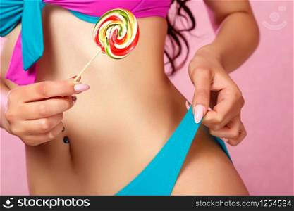 a young girl with a beautiful body dressed in a swimsuit holds a colorful bright Lollipop. on a pink isolated background.