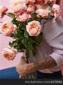 A young girl with a tattoo holds a vase with elegant pink roses on a pink background copy space. Mothers Day. A large bouquet of fresh pink roses in a glass vase holds a girl statue on a pink background. Valentine's Day Gift