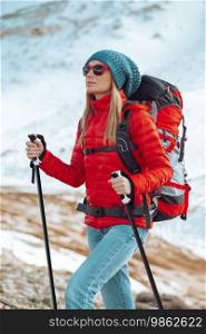 A young girl with long hair is engaged in winter tourism in the snowy mountains. Walking poles help her overcome snow-covered mountain slopes.. Active Woman with Walking Poles in the Mountains