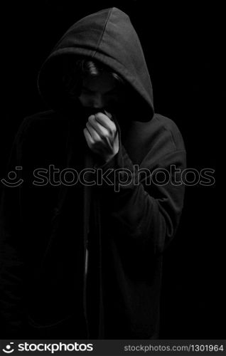 a young guy in a black hoodie on a black background with his face covered.