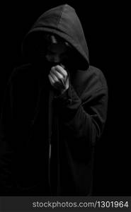 a young guy in a black hoodie on a black background with his face covered.