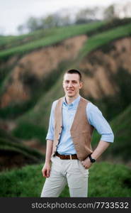 a young guy in a brown suit on the background of mountain green slopes near the old riverbed