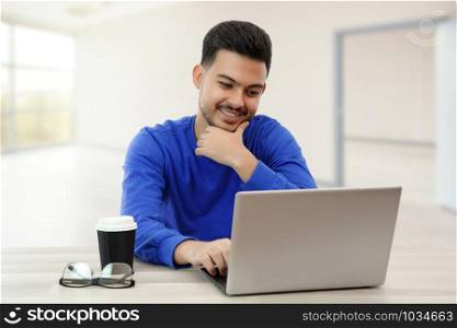 a young guy sitting at a laptop in search of work on the Internet , doing business in the global network with a Cup of coffee. on light background