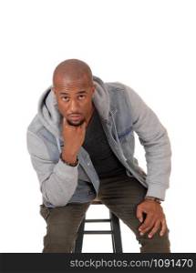 A young handsome African American man sitting on a chair with his fingers on his mouths, thinking, isolated for white background