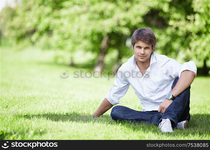 A young handsome man sits on the lawn