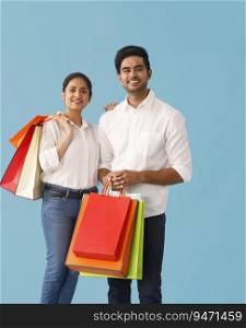 A YOUNG HAPPY COUPLE STANDING TOGETHER WHILE HOLDING SHOPPING BAGS