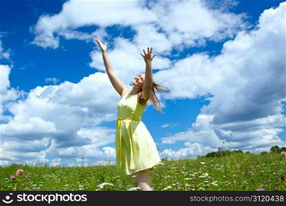A young happy girl with streaming in the wind hair, in a yellow dress, is throwing in the air camomile petals and smiling. Freedom concept.