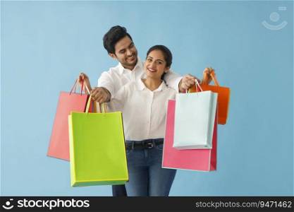 A YOUNG HUSBAND AND LOOKING AT WIFE WHILE POSING TOGETHER WITH SHOPPING BAGS