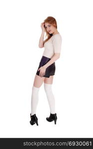 A young lovely brunette woman standing over white background inblack leather shorts and long white socks and high heels