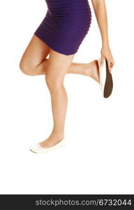 A young lovely woman fixing her shoe, standing from the front for whitebackground, looking down to her shoe, in a short lilac dress.