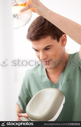 A young male dentist at work adjusting chair and light