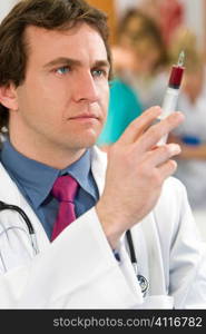 A young male doctor prepares a syringe with other medical staff out of focus in the background