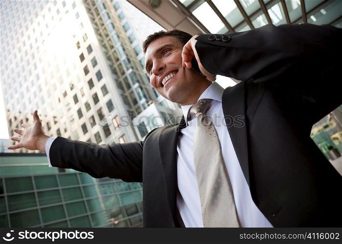 A young male executive celebrating success on his cell phone in front of a high rise office block in a modern city