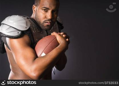 A young male football player athlete holds ball wearing shoulder pads