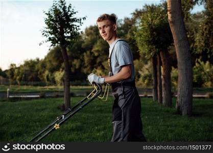 A young male gardener in overalls uses a lawn mower.Man mows the lawn with a lawn mower.Gardening and lawn mowing concept. A young male gardener in overalls uses a lawn mower.