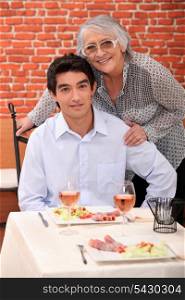 a young man and an old woman at the restaurant posing for the camera