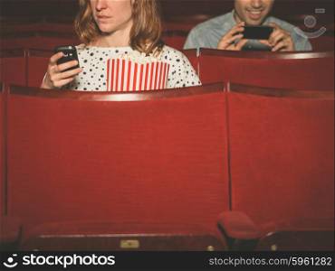 A young man and woman are using their phones in a movie theater
