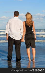A young man and woman celebrating arms raised and holding hands as a romantic couple on a beach with a bright blue sky