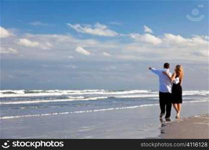 A young man and woman couple having a romantic walk on a beach with a bright blue sky