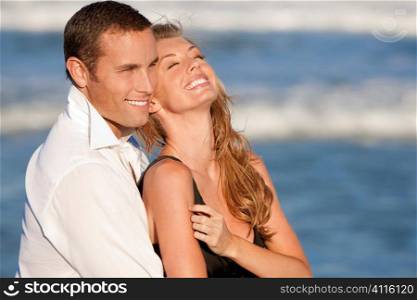 A young man and woman embracing and laughing as a happy romantic couple on a beach