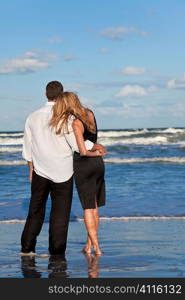 A young man and woman embracing as a romantic couple on a beach with a bright blue sky