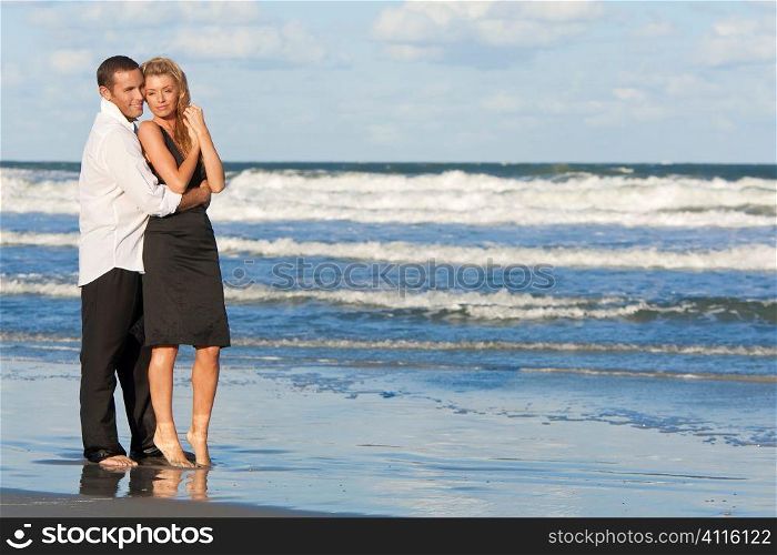 A young man and woman embracing as a romantic couple standing in the sea on a beach with a blue sky