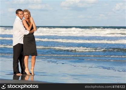 A young man and woman embracing as a romantic couple standing in the sea on a beach with a blue sky