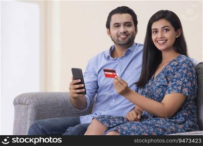 A young man and woman sitting in a room holding a smart phone and credit card .
