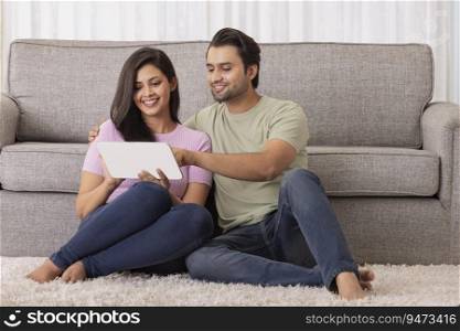 A young man and woman sitting in their room working on tablet phone.