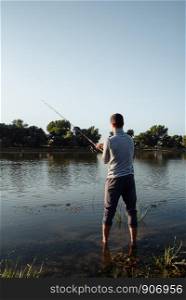 A young man catches a fish by the river. A man fisherman on the river bank catches a fish