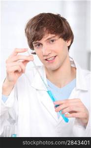 A young man extracting a sample of liquid from a testing tube.