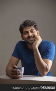 A YOUNG MAN HAPPILY LOOKING AWAY WHILE HOLDING COFFEE MUG