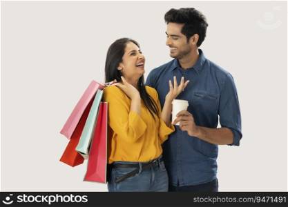 A YOUNG MAN HAPPILY LOOKS AT WIFE WHILE SHE LAUGHS HOLDING SHOPPING BAGS IN HAND