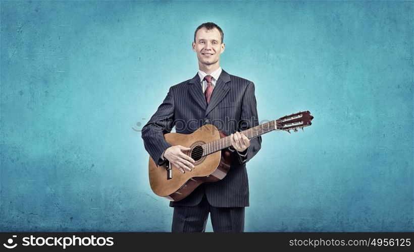 A young man in a black suit playing acoustic guitar. Man play guitar