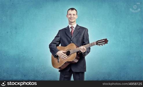 A young man in a black suit playing acoustic guitar. Man play guitar