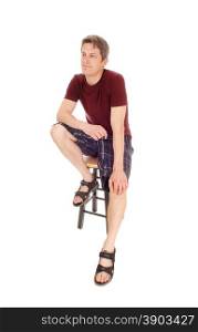 A young man in a burgundy t-shirt and shorts sitting relaxed on a chair,isolated for white background.