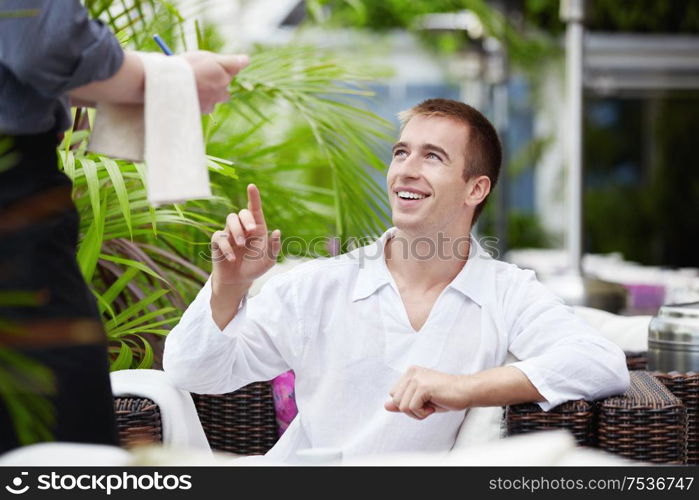 A young man in a cafe makes an order to the waiter